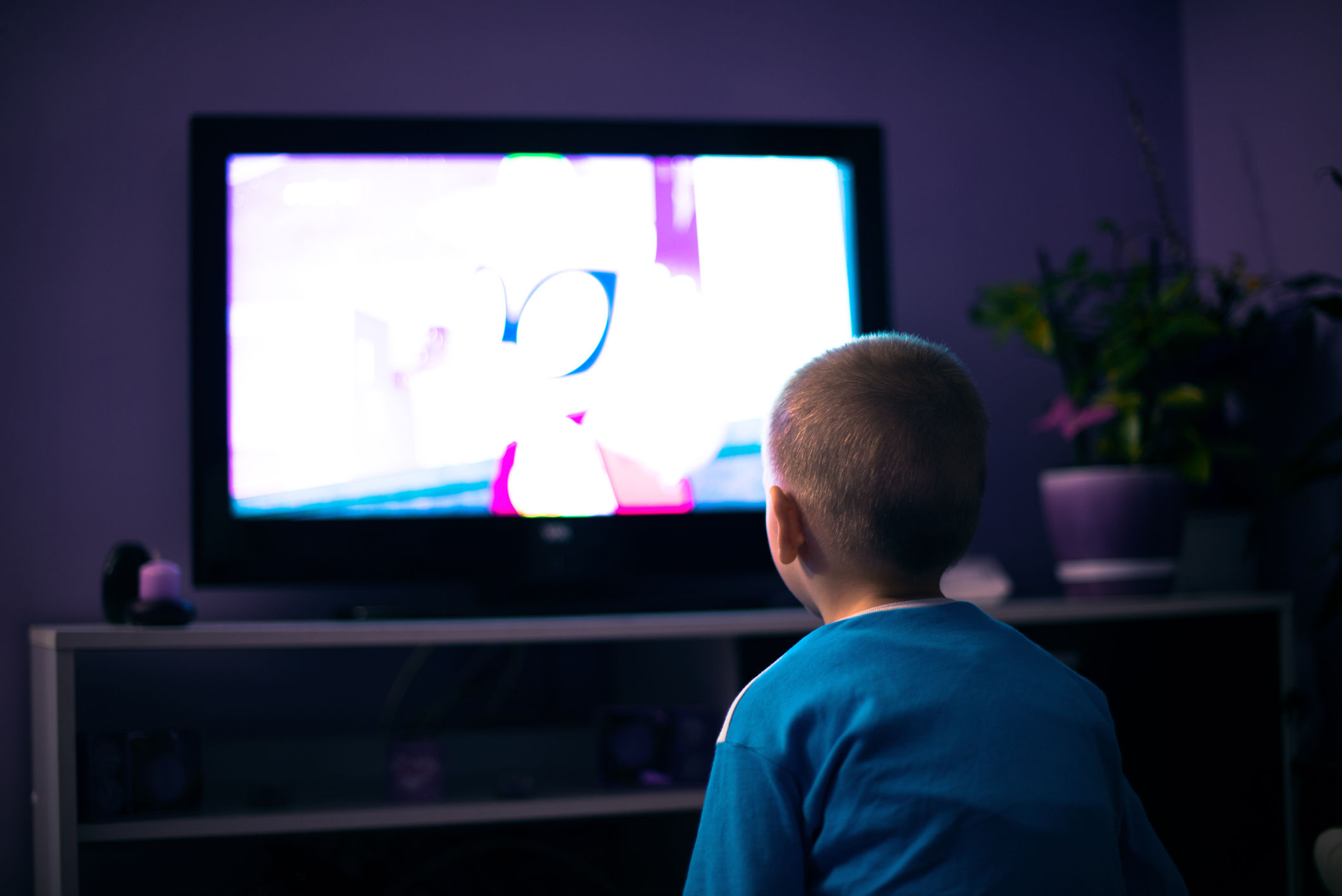Photo d'un enfant assis dans le noir devant un écran TV diffusant un dessin animé