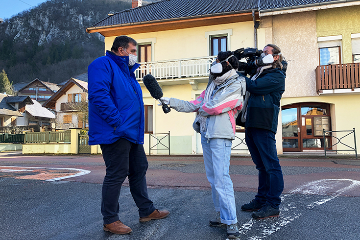 Le maire de La Balme-de-Sillingy, Francois Daviet, portant un masque, parle avec deux journalistes (un homme et une femme, masquées tous deux) qui tiennent à la main caméra et micro.