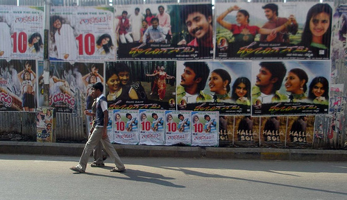 Deux personnes marchent devant un mur recouvert d'affiches de films en Inde